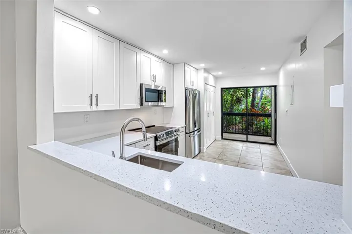 Kitchen featuring light stone counters, stainless steel appliances, recessed lighting, visible vents, and a sink