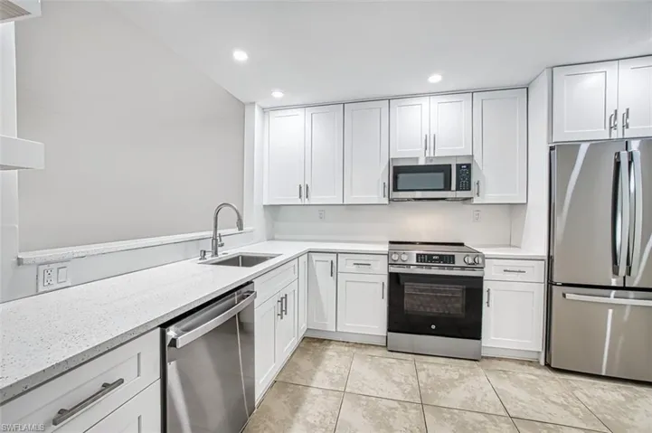 Kitchen with white cabinets, light stone counters, appliances with stainless steel finishes, a sink, and recessed lighting
