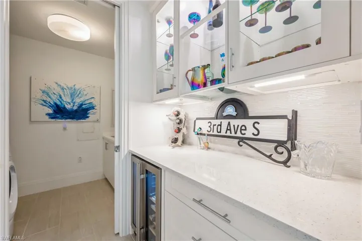 Bar featuring white cabinets, light stone countertops, wine cooler, and tasteful backsplash