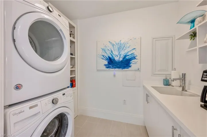 Laundry room featuring sink, light tile patterned flooring, cabinets, and stacked washer and clothes dryer