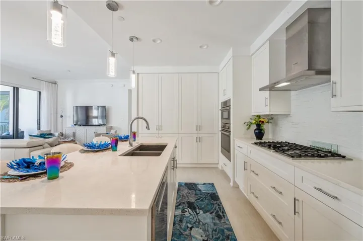 Kitchen featuring wall chimney exhaust hood, light stone countertops, decorative light fixtures, open floor plan, and white cabinets