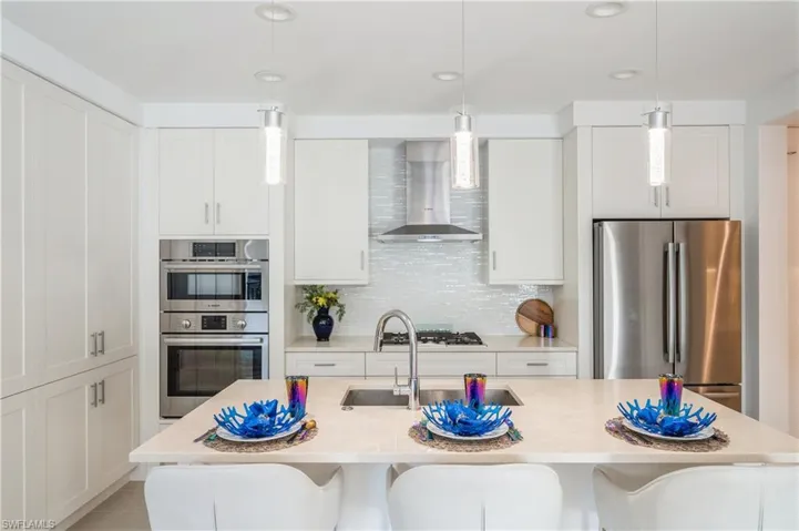 Kitchen with decorative backsplash, appliances with stainless steel finishes, white cabinetry, and wall chimney exhaust hood