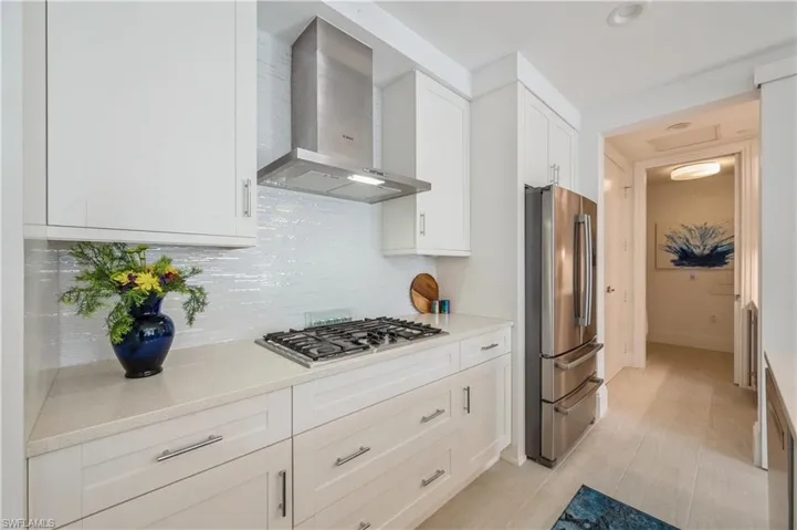 Kitchen with stainless steel appliances, white cabinetry, tasteful backsplash, and wall chimney exhaust hood