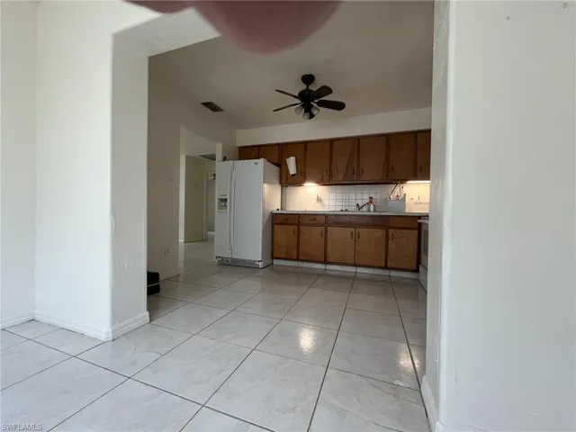 Kitchen featuring a ceiling fan, backsplash, white refrigerator with ice dispenser, brown cabinetry, and light tile patterned floors