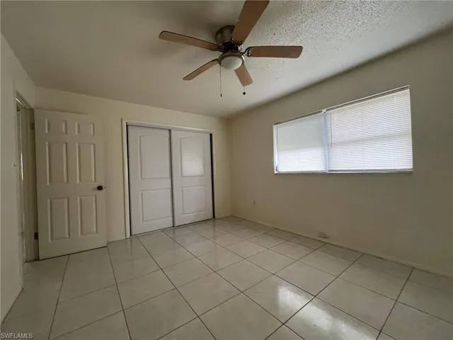 Unfurnished bedroom with ceiling fan, light tile patterned flooring, a closet, and a textured ceiling