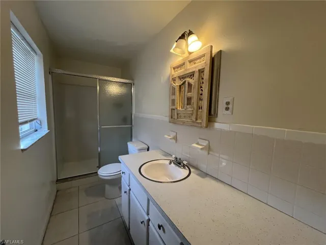 Full bathroom with vanity, a stall shower, tile patterned floors, toilet, and tile walls