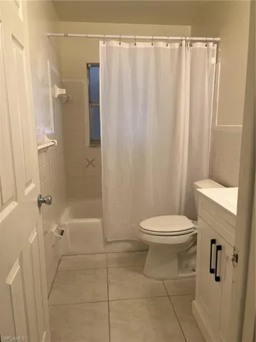 Full bathroom featuring tile walls, toilet, shower / tub combo, tile patterned floors, and vanity