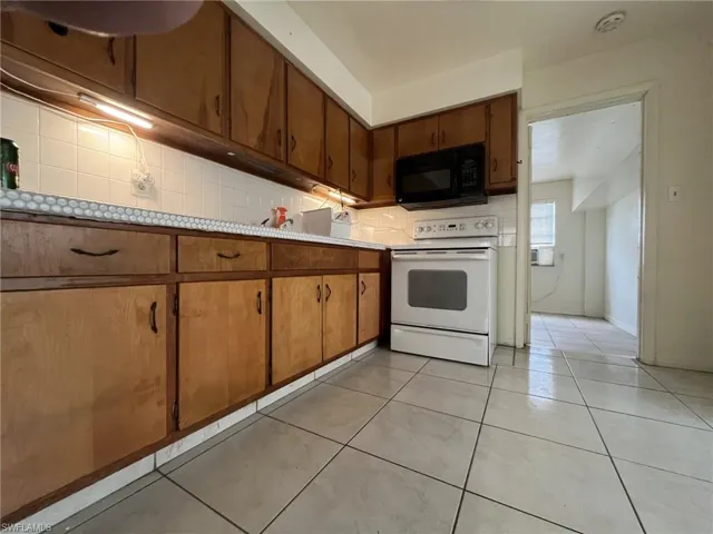 Kitchen featuring light tile patterned floors, decorative backsplash, black microwave, white electric range, and brown cabinets