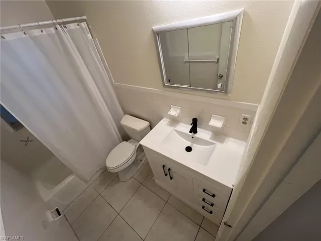 Full bath featuring vanity, a wainscoted wall, tile patterned flooring, tile walls, and toilet