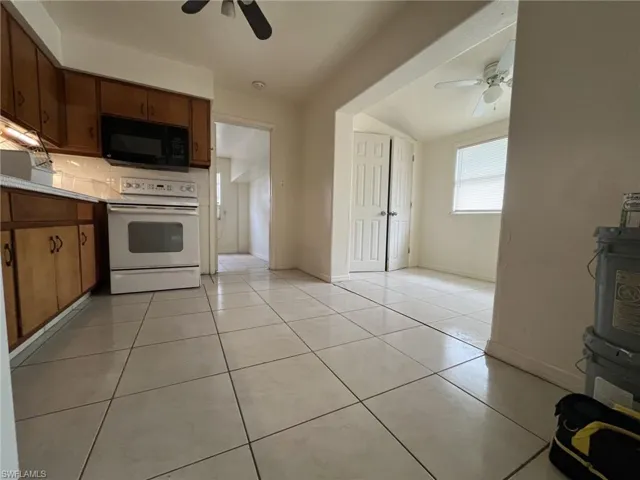 Kitchen featuring tasteful backsplash, black microwave, light tile patterned flooring, white electric stove, and a ceiling fan