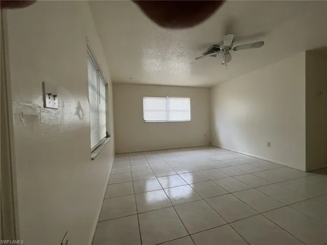 Empty room featuring a textured ceiling, light tile patterned flooring, and a ceiling fan