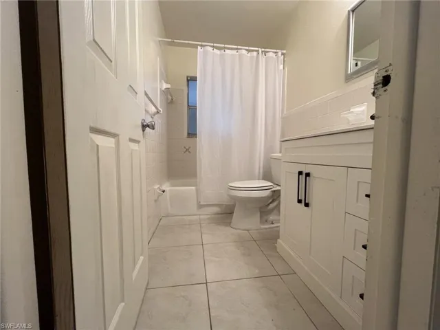 Full bath featuring tile patterned floors, shower / bath combination with curtain, toilet, and vanity