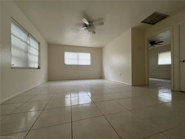 Empty room with light tile patterned floors, baseboards, a textured ceiling, and ceiling fan