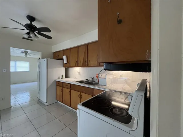 Kitchen featuring tasteful backsplash, light tile patterned floors, white appliances, a ceiling fan, and a sink