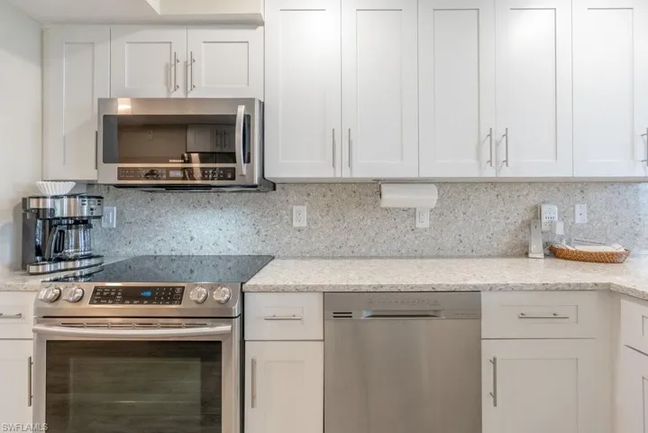Kitchen with light stone counters, appliances with stainless steel finishes, decorative backsplash, and white cabinetry
