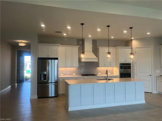 Kitchen featuring stainless steel appliances, white cabinetry, pendant lighting, and tasteful backsplash
