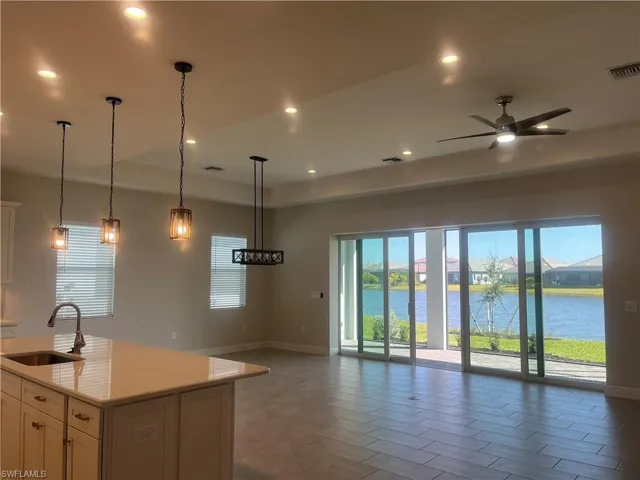 Kitchen with a ceiling fan, hanging light fixtures, open floor plan, a center island with sink, and light stone countertops