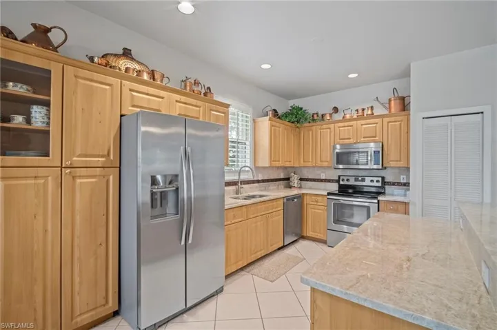 Kitchen featuring stainless steel appliances, light tile patterned floors, light stone counters, decorative backsplash, and light brown cabinets