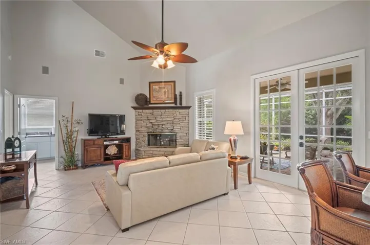 Living room featuring high vaulted ceiling, a fireplace, ceiling fan, light tile patterned flooring, and french doors