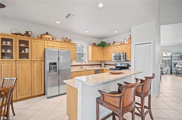 Kitchen featuring appliances with stainless steel finishes, a kitchen bar, light brown cabinetry, a center island, and backsplash