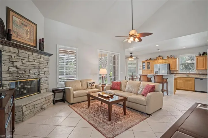 Living room featuring light tile patterned flooring, a fireplace, a ceiling fan, and high vaulted ceiling
