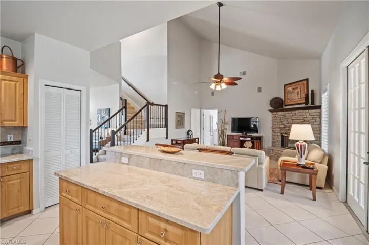 Kitchen featuring light tile patterned flooring, high vaulted ceiling, a fireplace, open floor plan, and light stone counters