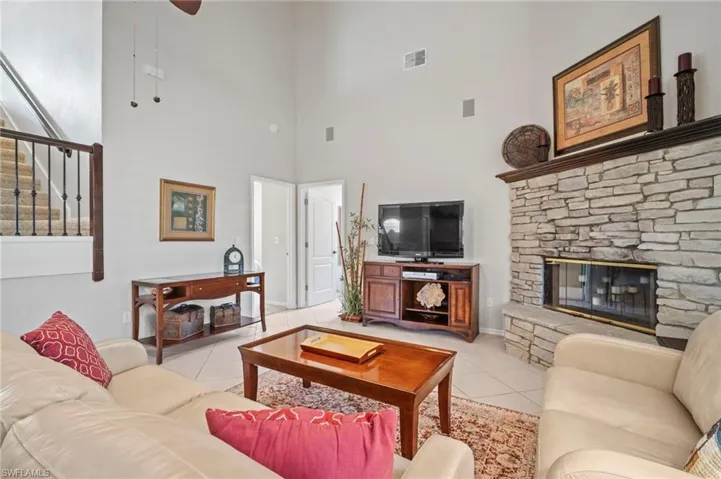 Living room featuring a fireplace, light tile patterned floors, stairway, a high ceiling, and ceiling fan