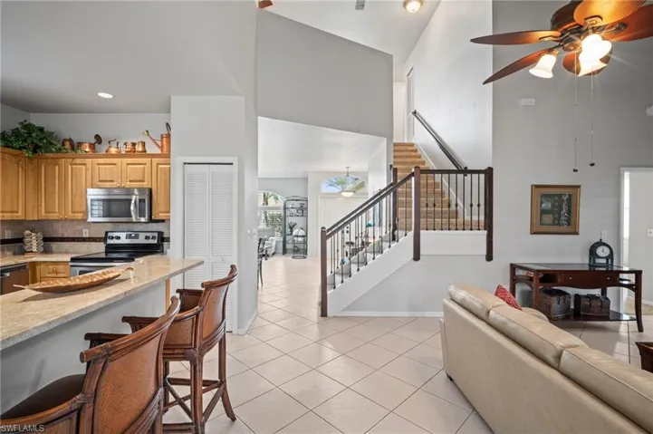 Living area featuring a ceiling fan, light tile patterned floors, stairs, and a high ceiling