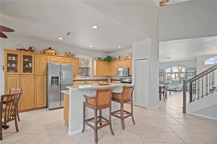 Kitchen featuring a breakfast bar, stainless steel appliances, a kitchen island with sink, recessed lighting, and glass insert cabinets