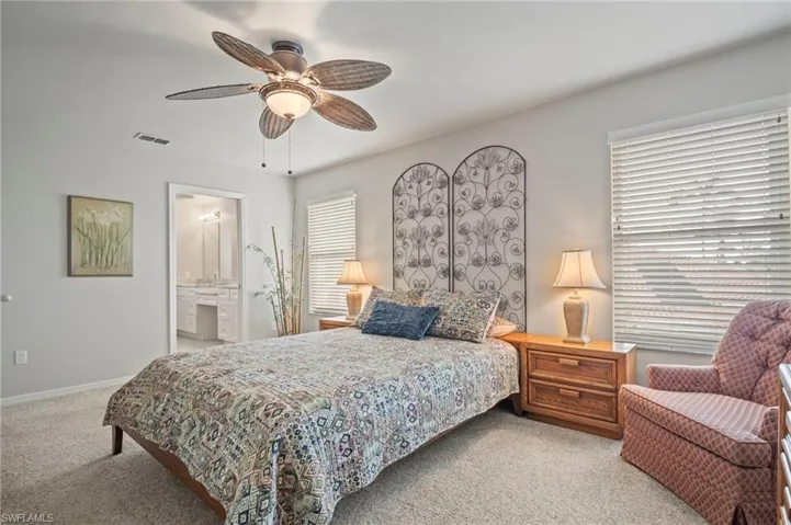 Bedroom with light colored carpet, ceiling fan, and connected bathroom
