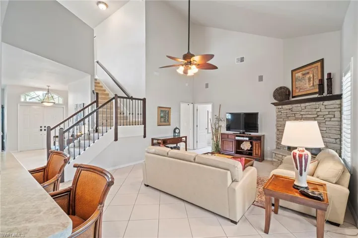 Living area featuring stairway, high vaulted ceiling, plenty of natural light, light tile patterned floors, and ceiling fan