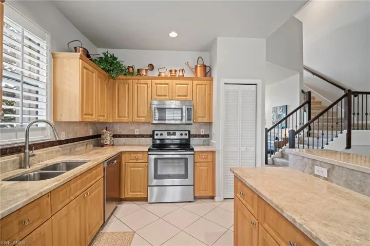 Kitchen with appliances with stainless steel finishes, tasteful backsplash, light tile patterned flooring, light stone counters, and recessed lighting