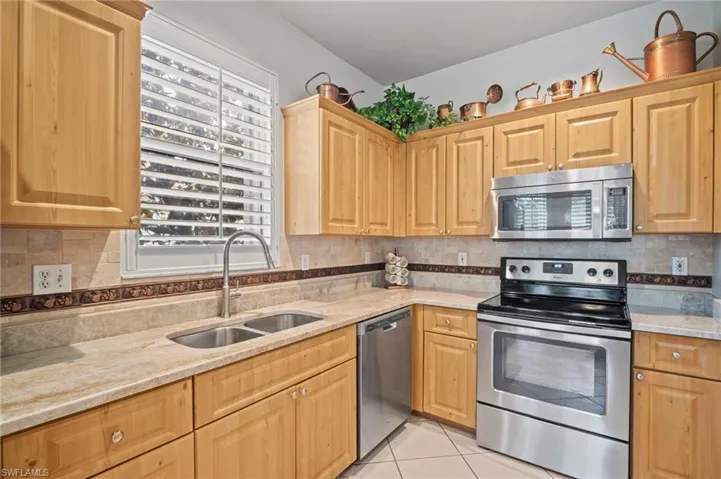 Kitchen with appliances with stainless steel finishes, tasteful backsplash, light tile patterned floors, and light stone counters