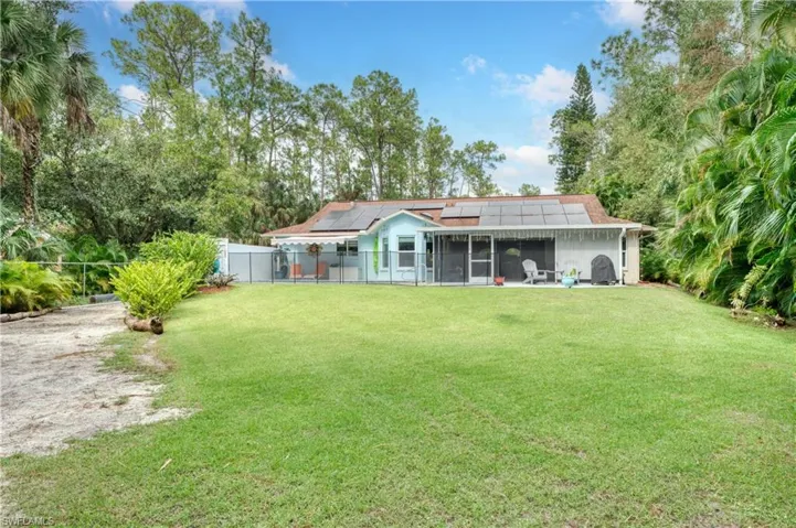 Back of property with a sunroom, a lawn, and solar panels