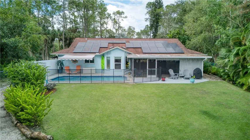 Rear view of property featuring a patio, a fenced in pool, a lawn, and solar panels