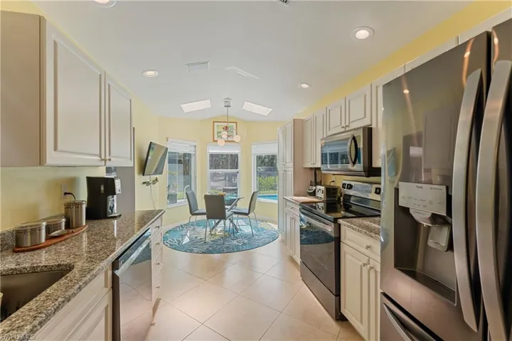 Kitchen featuring light stone counters, stainless steel appliances, decorative light fixtures, lofted ceiling with skylight, and tile floors