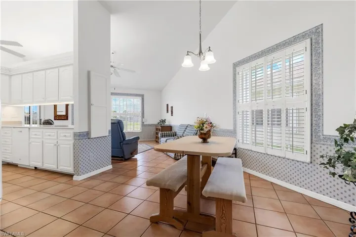 Dining area featuring ceiling fan, wallpapered walls, high vaulted ceiling, a chandelier, and light tile patterned floors