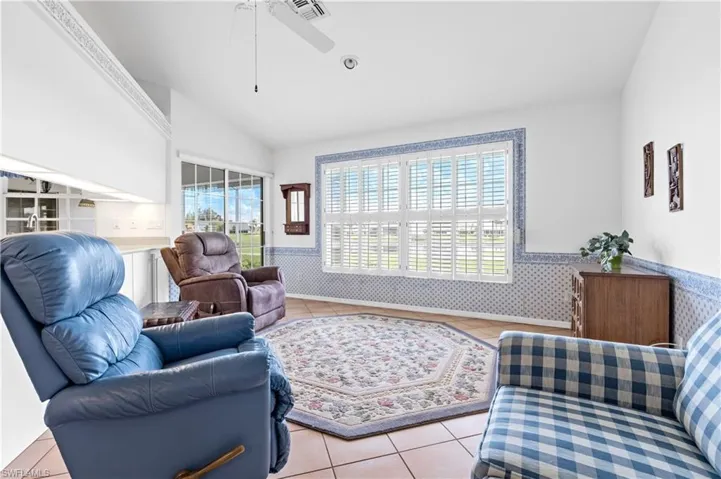 Living area featuring wainscoting, healthy amount of natural light, light tile patterned floors, vaulted ceiling, and ceiling fan