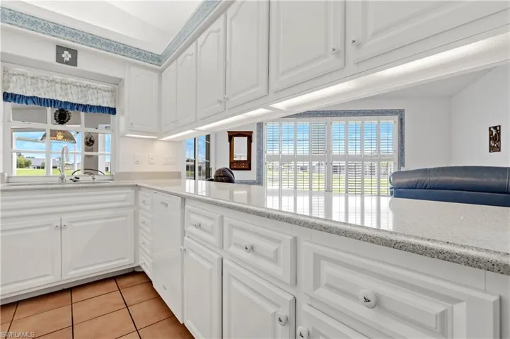 Kitchen with dishwasher, light tile patterned floors, white cabinets, and light stone counters
