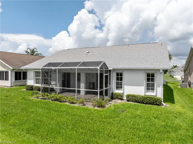 Rear view of property featuring a yard, stucco siding, and a shingled roof