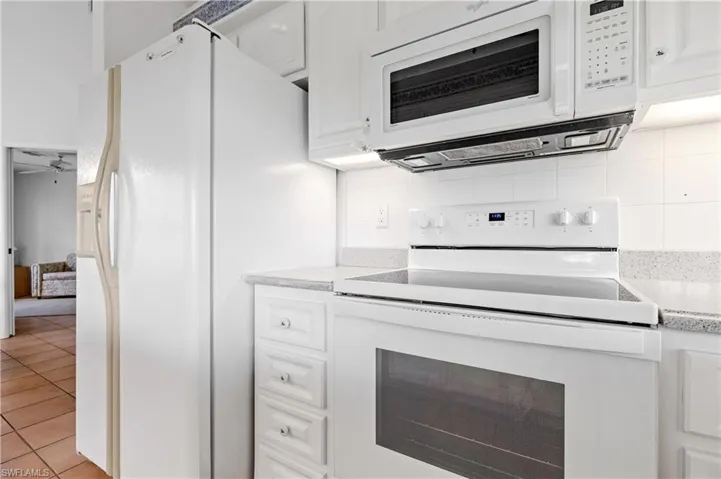 Kitchen with white appliances, light countertops, backsplash, white cabinetry, and light tile patterned flooring