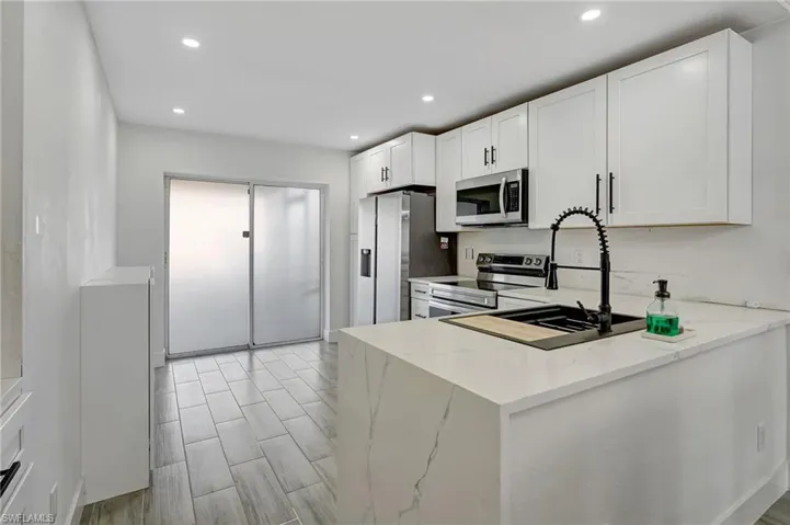 Kitchen with stainless steel appliances, white cabinetry, wood tiled floors, light stone countertops, and recessed lighting