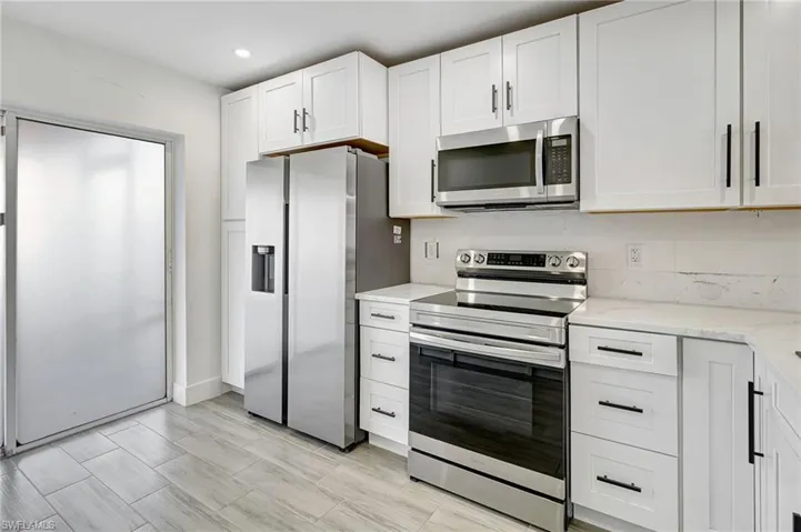 Kitchen featuring appliances with stainless steel finishes, white cabinetry, light stone countertops, and recessed lighting