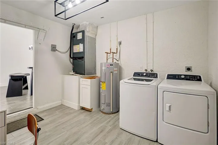 Laundry room with wood tiled floors, water heater, heating unit, and washer and clothes dryer