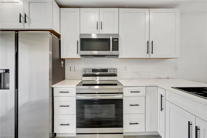 Kitchen featuring stainless steel appliances, white cabinets, and light stone counters