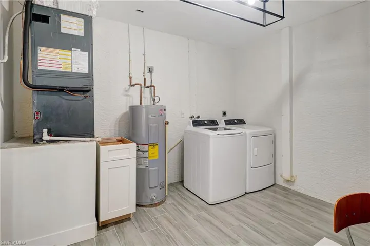 Laundry room with a textured wall, heating unit, washing machine and dryer, electric water heater, and wood finish floors