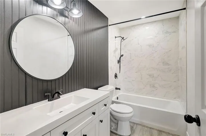 Bathroom featuring shower / bathtub combination, vanity, light wood finished floors, and wood walls