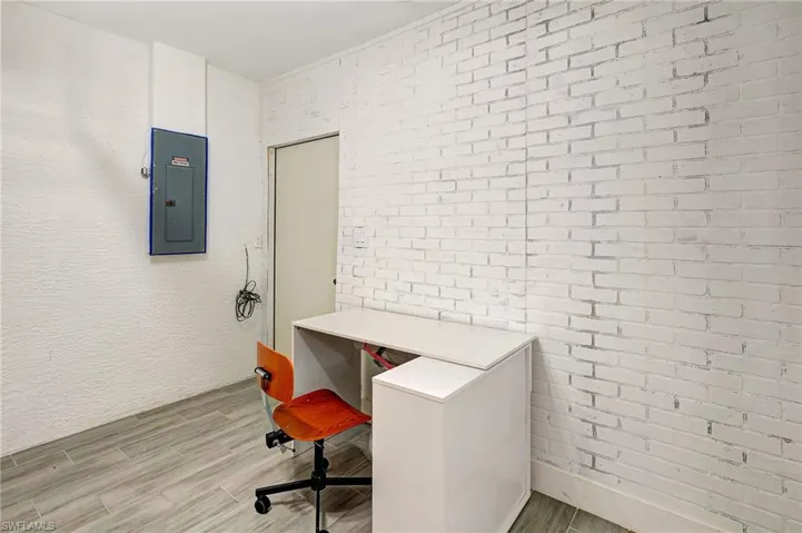 Office featuring wood tiled floors, electric panel, a textured wall, and brick wall