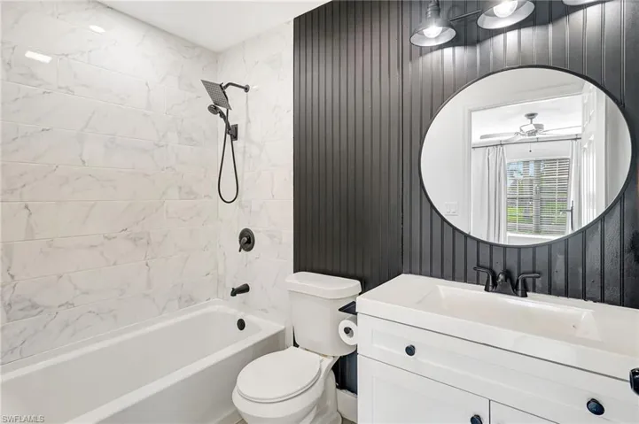 Bathroom with shower / tub combination, vanity, wood walls, and a ceiling fan