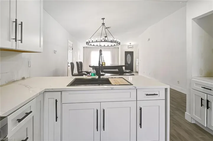 Kitchen featuring white cabinets, a peninsula, light stone countertops, and dark wood finished floors